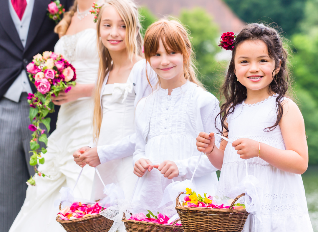 Neben dem Brautpaar stehen drei weitere junge Mädchen in weiß gekleidet als Blumenkinder am Altar