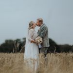 Frisch vermähltes Ehepaar schießt Hochzeitsfotos auf einer Wiese mit hohem Gras und gibt sich einen Kuss 