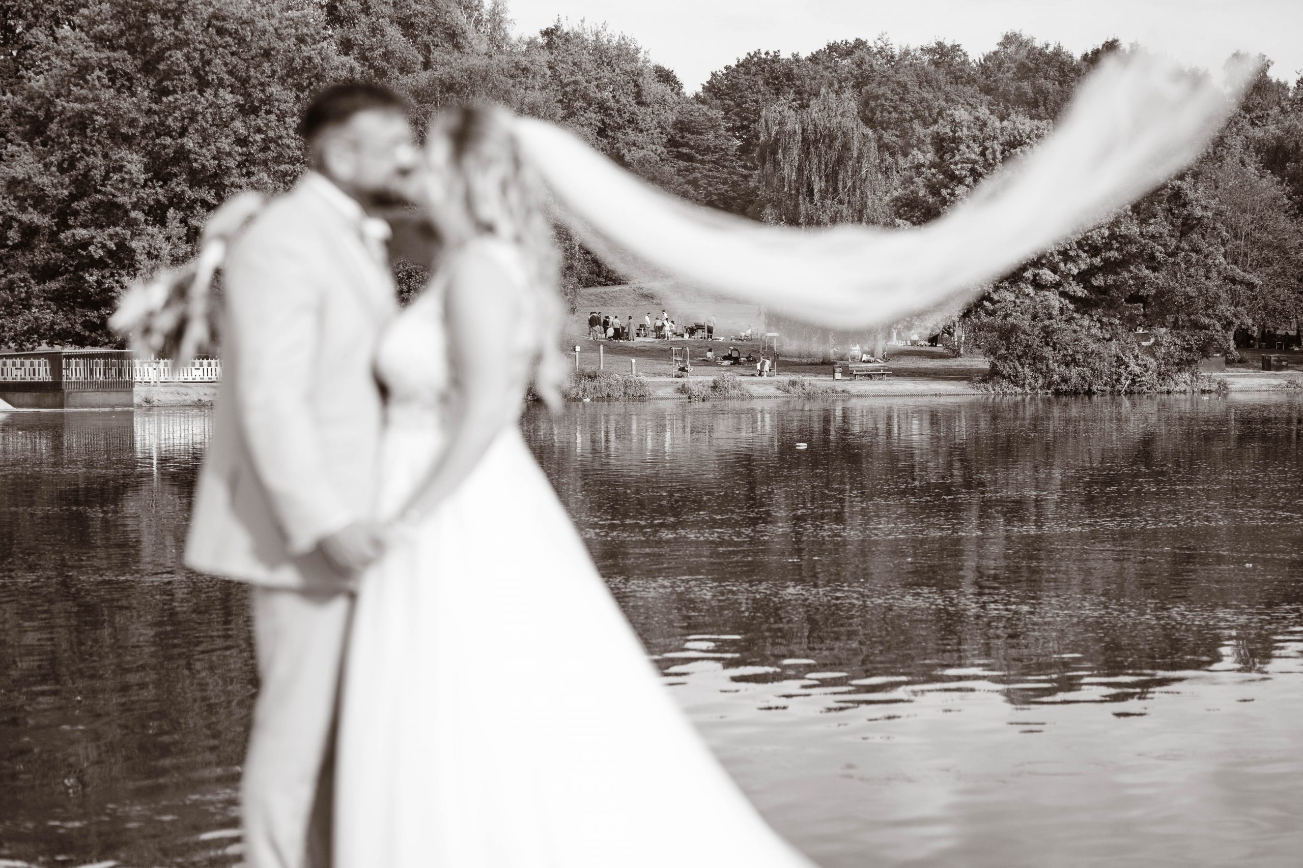 Schwarz-Weißes Bild von dem Brautpaar, wie sie sich am See einen Kuss geben