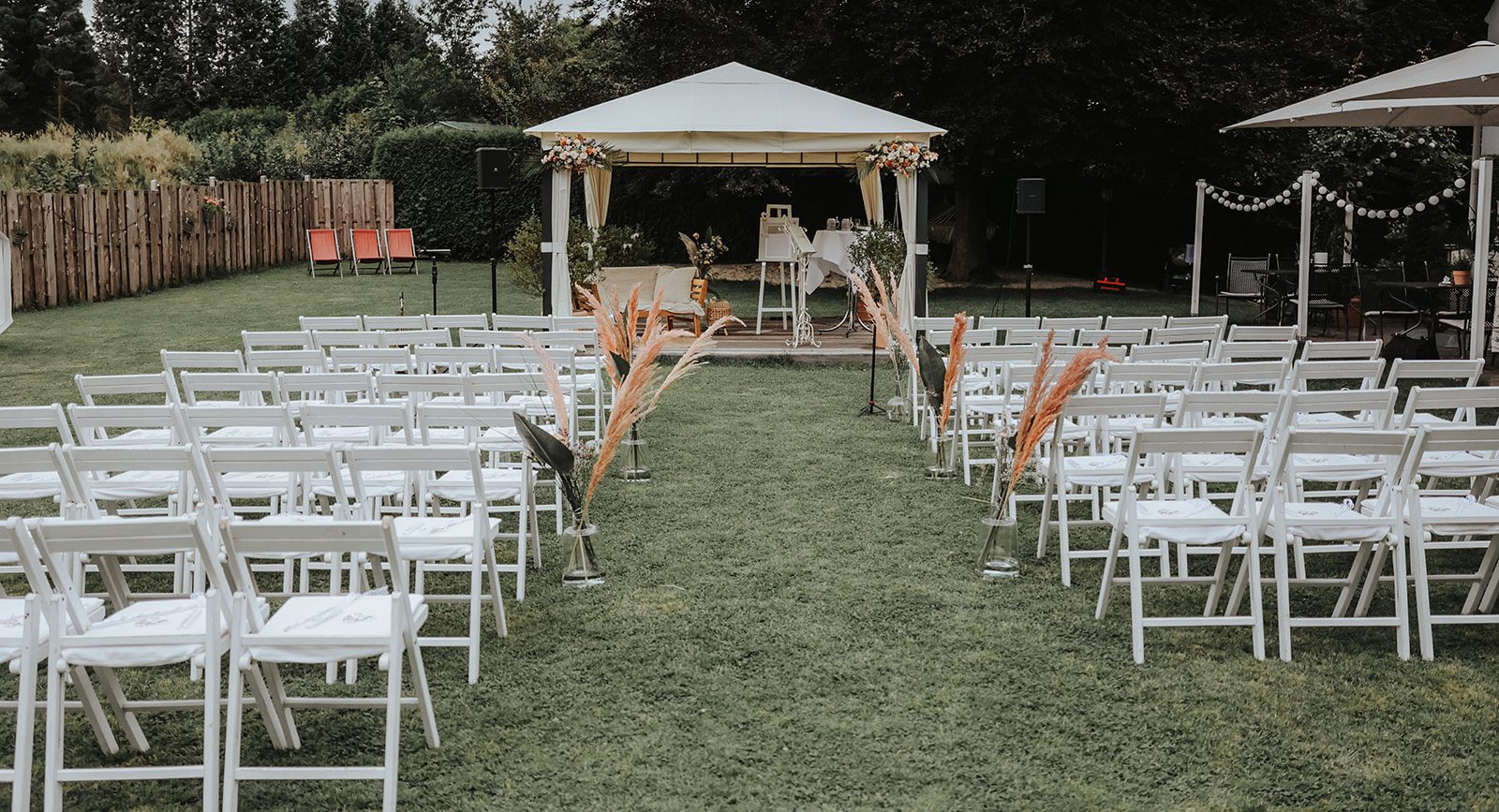 Trauort der Location Lennhof in Dortmund ist unüberdacht auf einer Wiese. Stühle sind dekoriert mit Orangenen Trockenblumen